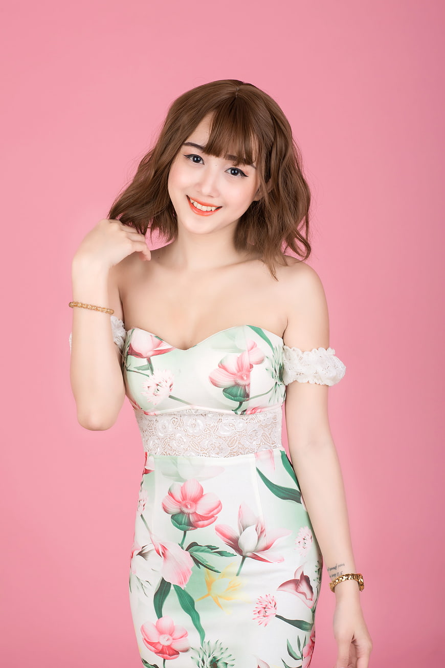 Smiling young woman in floral dress against pink studio background