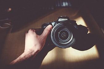 Hand holding Canon DSLR camera on wooden table