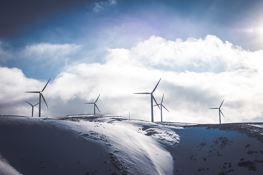 Wind turbines on snowy hill against blue sky