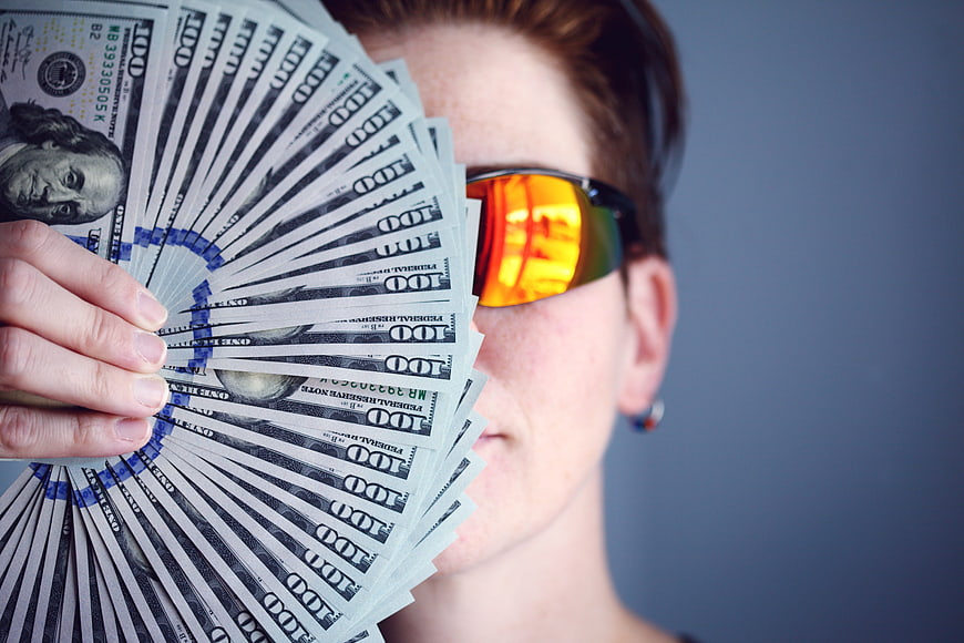 Woman holding fan of US hundred dollar bills with orange sunglasses