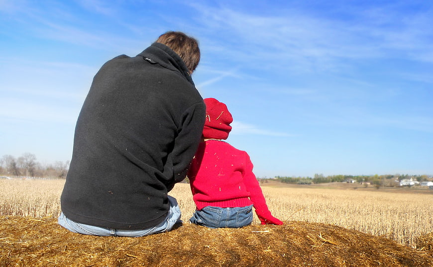 Father and son sitting on hay bale in field