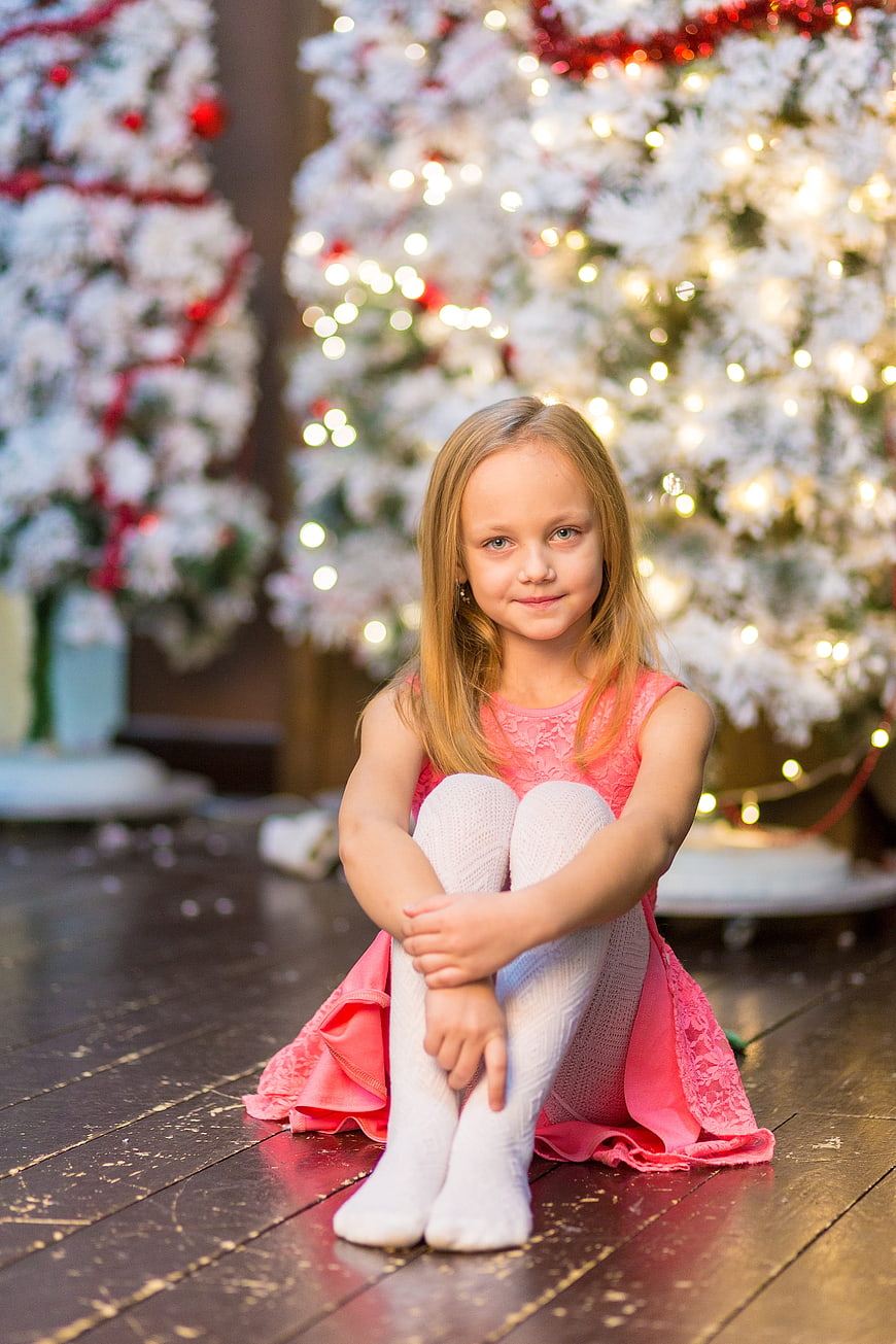 Cute Girl in Pink Dress Sitting by Christmas Tree
