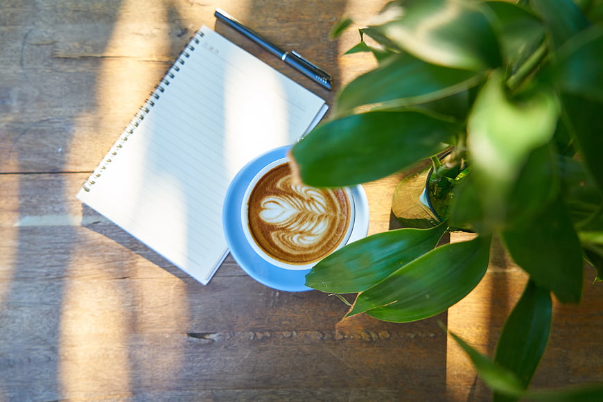 Flat lay of latte art coffee, notebook, and plant on wooden table