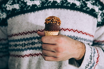 Hand holding chocolate ice cream cone in winter sweater