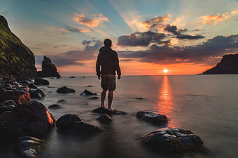 Man Standing on Rocks Watching Ocean Sunset