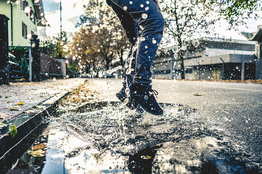 Man jumping in puddle on wet street with water splashes