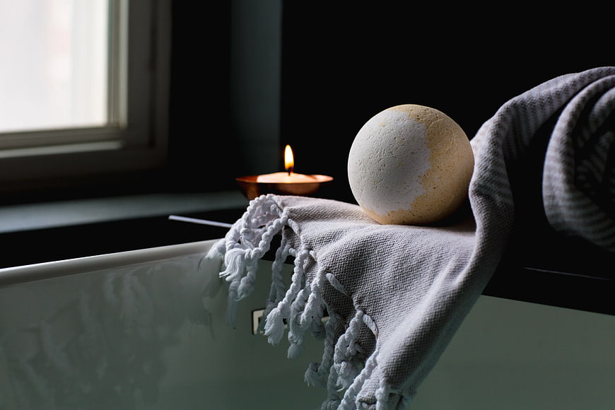 Bath Bomb and Candle on Bathtub Edge with Towel