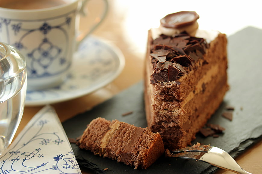 Slice of layered chocolate cake with coffee cup on slate