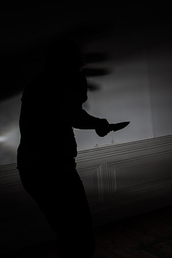 Silhouette of person holding knife in dark room