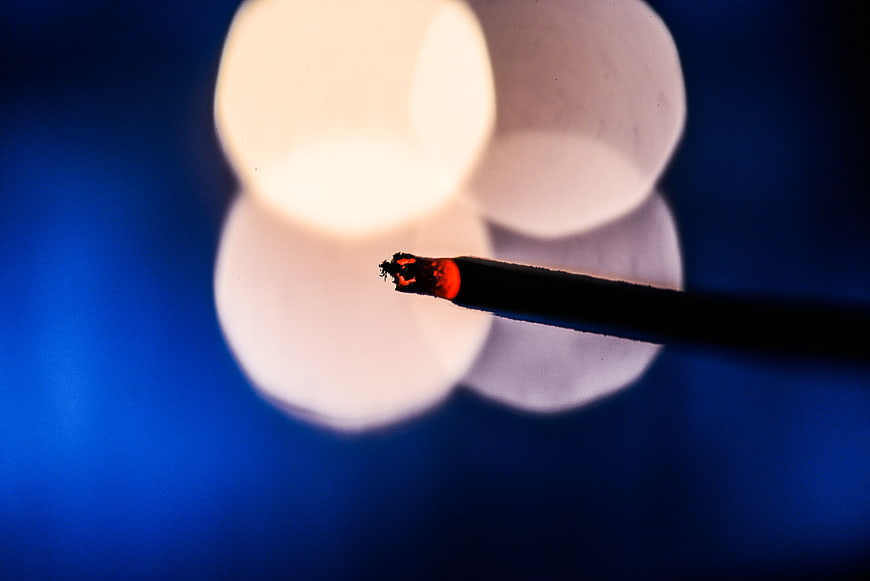 Close-up of burning cigarette tip with blue bokeh background