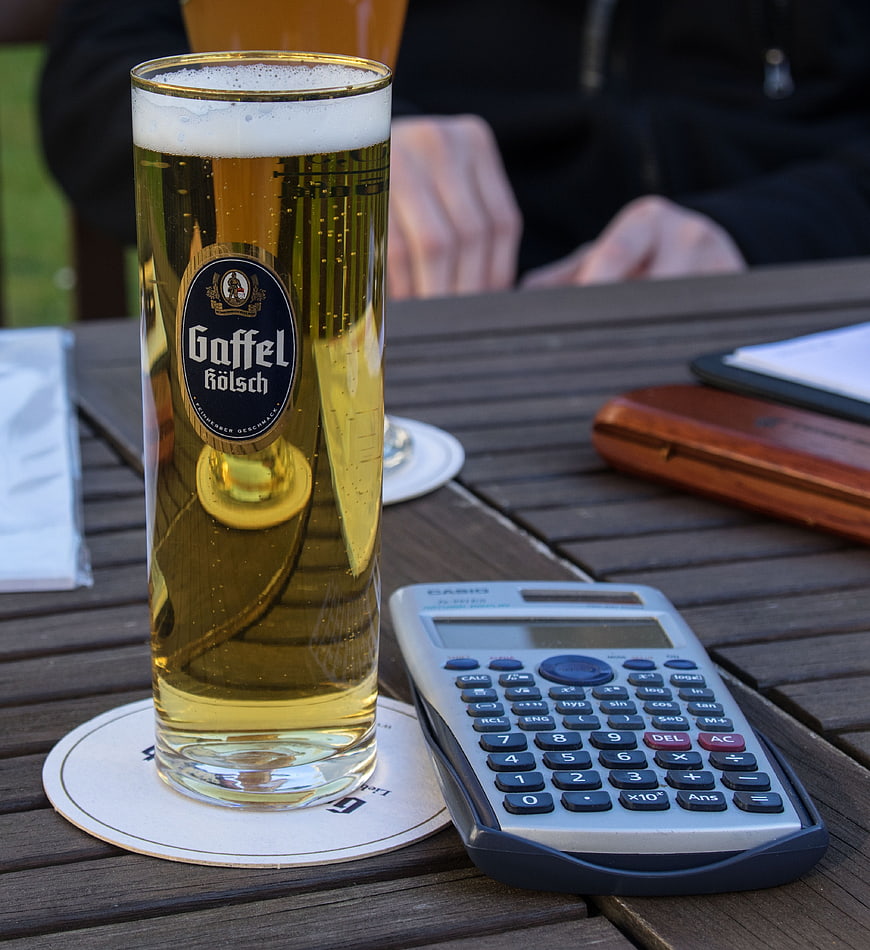 Gaffel Kölsch beer glass and calculator on wooden table