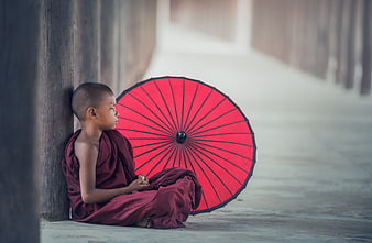 Young Buddhist Monk Sitting with Red Umbrella in Monastery