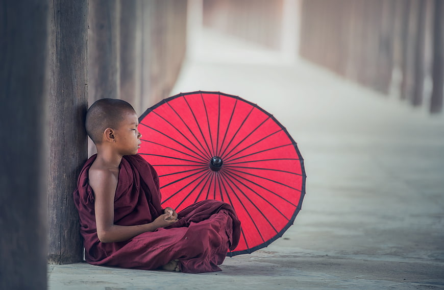 Young Buddhist Monk Sitting with Red Umbrella in Monastery