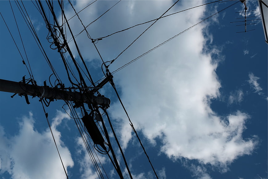 Silhouette of tangled power lines against blue sky with clouds