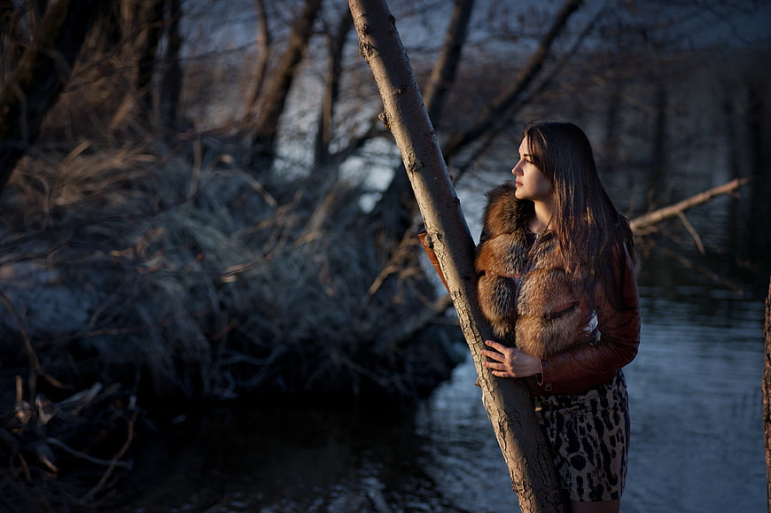 Woman in Fur Coat Standing by River in Winter Forest