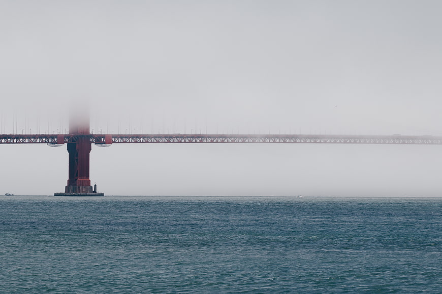 Red bridge tower emerging from thick fog over calm ocean water