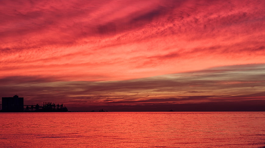 Dramatic Red Sunset Over Ocean with Silhouette of Port