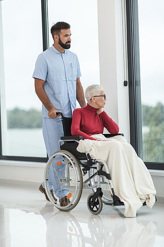 Male nurse pushing elderly woman in wheelchair near window