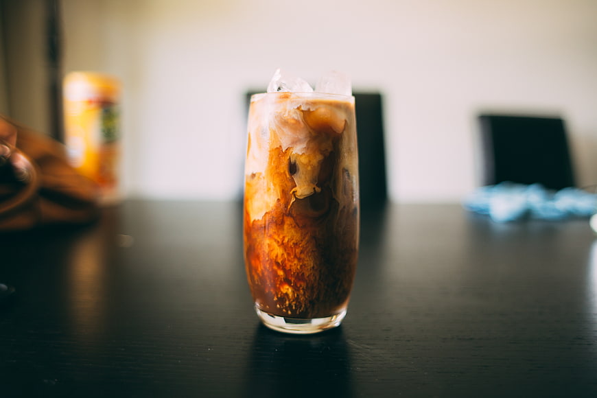 Iced Coffee with Swirling Milk in Glass on Dark Table