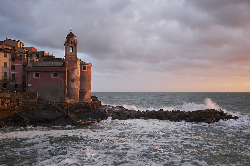 Dramatic coastal church with crashing waves at sunset