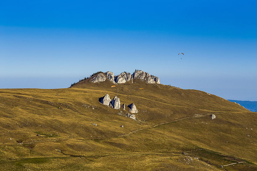 Paragliders soaring over golden mountain hills and rocky peaks