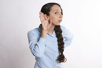 Young woman with braided hair listening intently with hand to ear