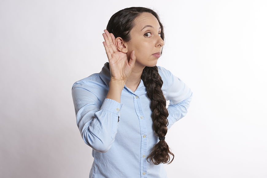 Young woman with braided hair listening intently with hand to ear
