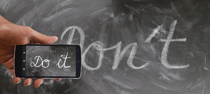 Hand holding smartphone with 'Do it' text over 'Don't' chalkboard background