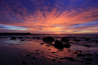 Vibrant Sunset Over Rocky Beach with Silhouetted Stones