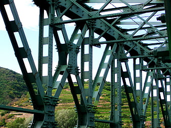 Green steel truss bridge structure with vineyard background