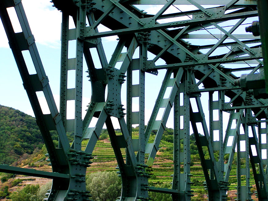 Green steel truss bridge structure with vineyard background