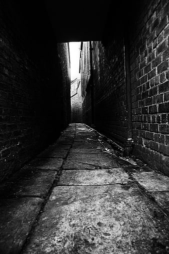 Dark narrow brick alleyway with cobblestone path leading to bright exit