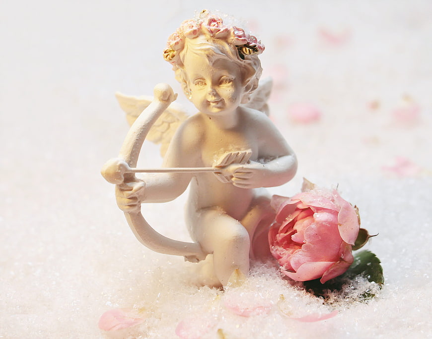 Cupid figurine with bow and arrow in snow with pink rose