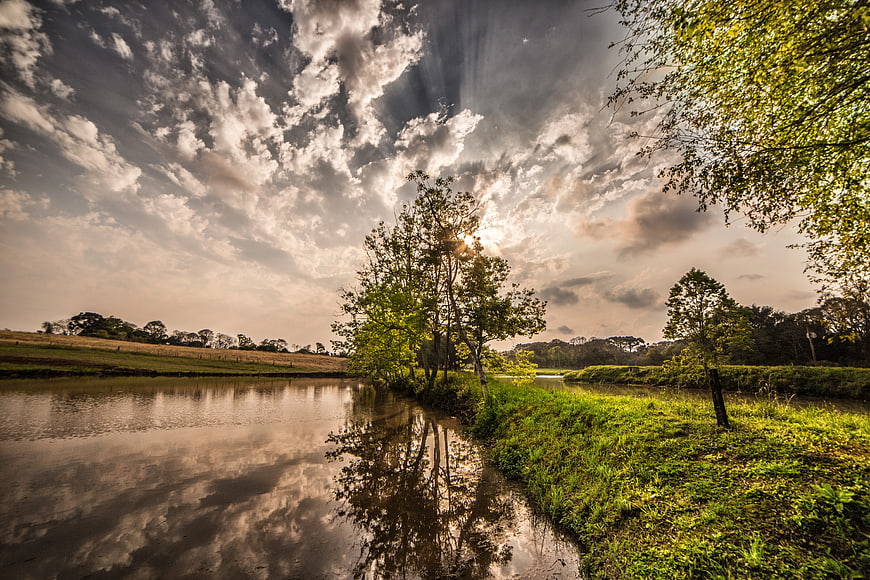Dramatic Sun Rays Over River and Green Trees
