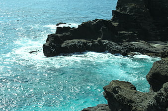 Turquoise ocean waves crashing against dark volcanic rocks