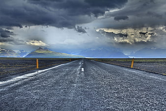 Dramatic wet road leading to mountains under stormy sky