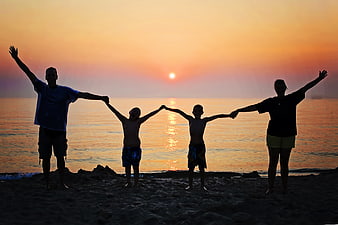 Happy family silhouette holding hands on beach at sunset