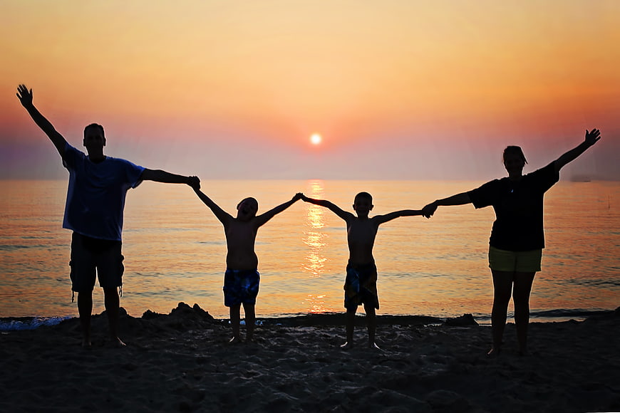 Happy family silhouette holding hands on beach at sunset