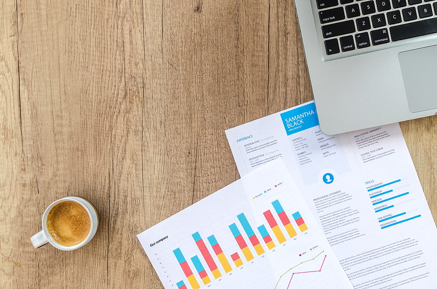 Flat lay of business documents, laptop, and coffee on wooden desk
