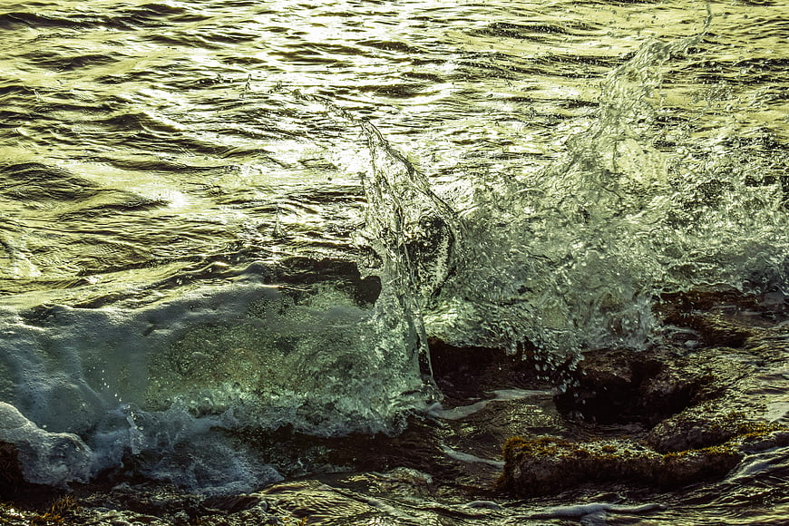 Dynamic ocean wave crashing on rocks with golden sunlight