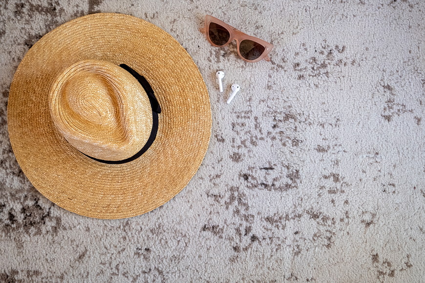 Summer vacation flat lay with straw hat, sunglasses, and wireless earbuds on textured background