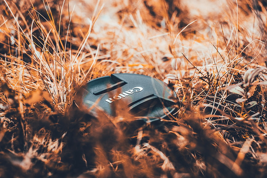 Canon lens cap resting in dry autumn grass