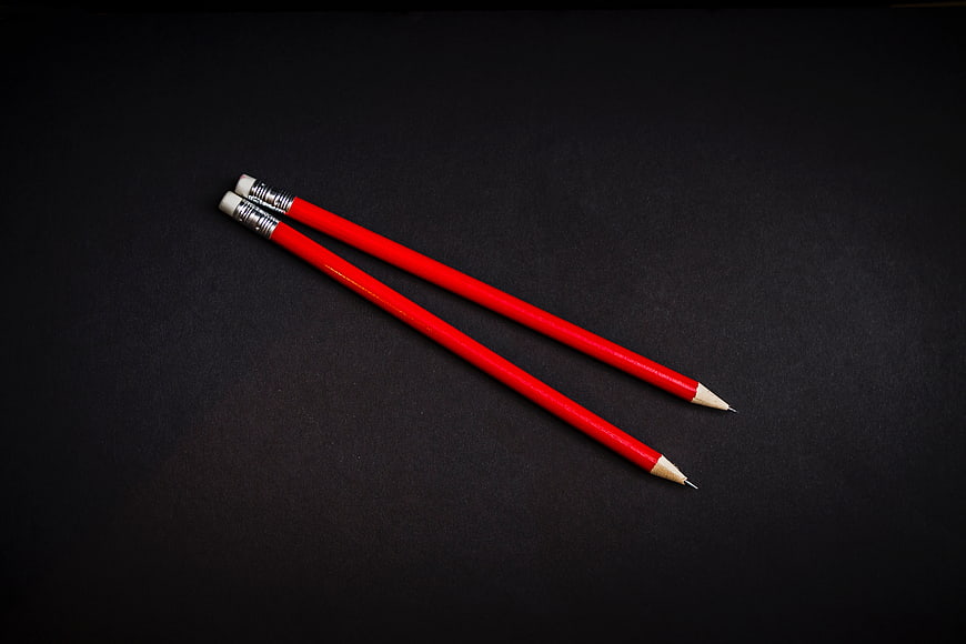 Two red pencils on black background