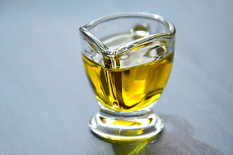 Glass gravy boat filled with golden olive oil on a gray surface