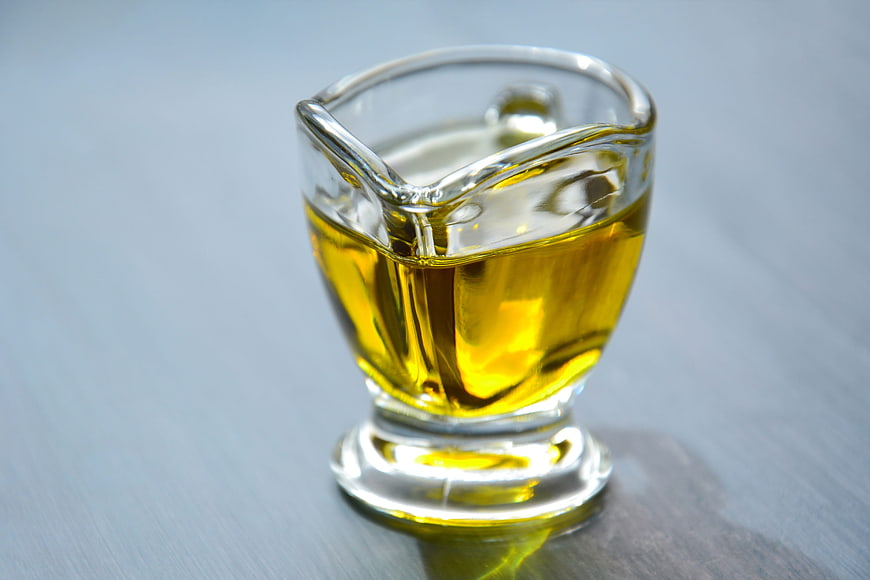 Glass gravy boat filled with golden olive oil on a gray surface