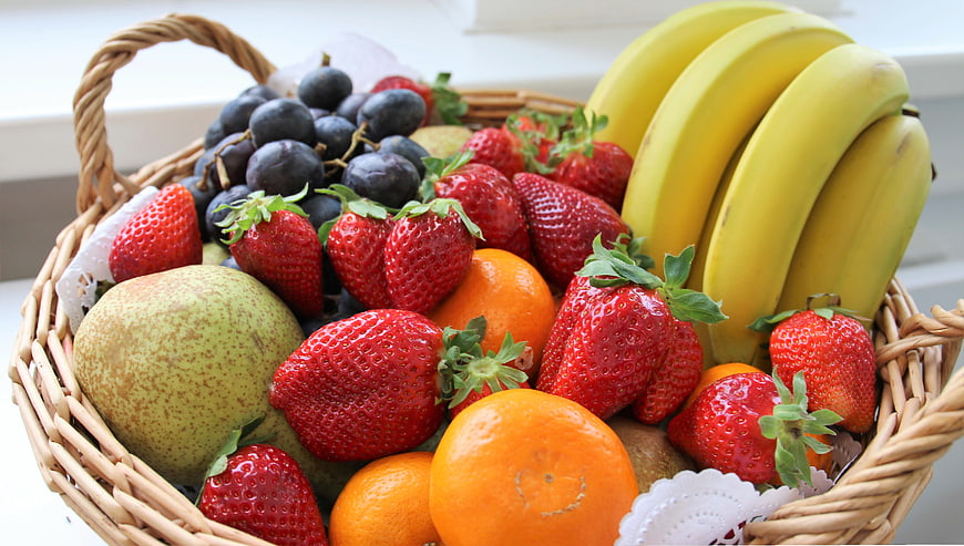 Wicker Basket Filled With Fresh Strawberries, Bananas, Oranges, And Grapes