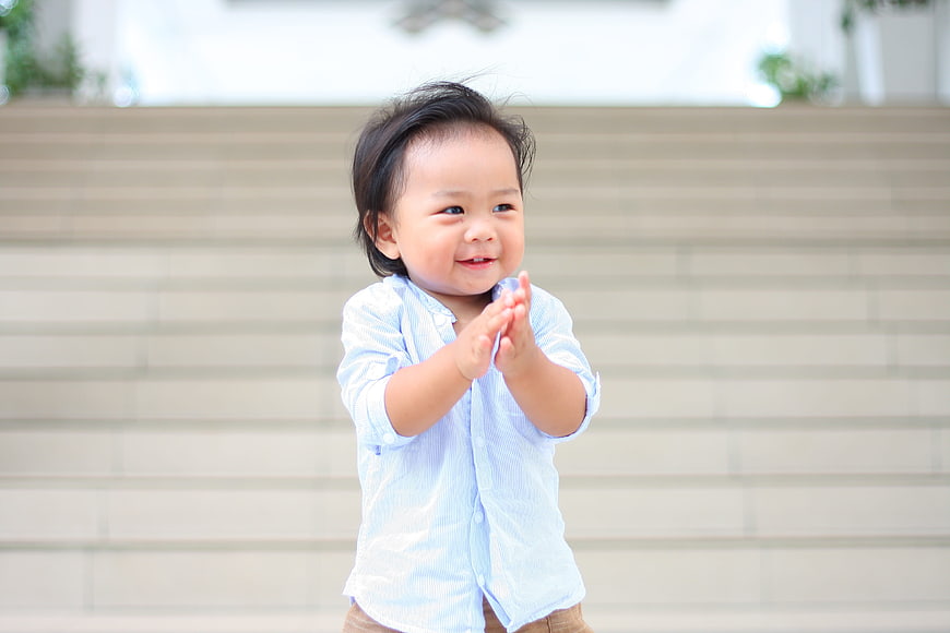 Happy toddler boy clapping hands in front of stairs