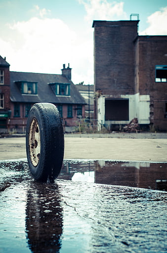 Lone tire standing in puddle with urban decay background
