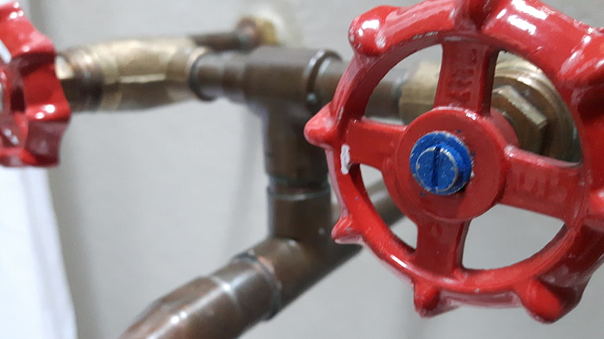 Close-up of red industrial water valve on copper pipes