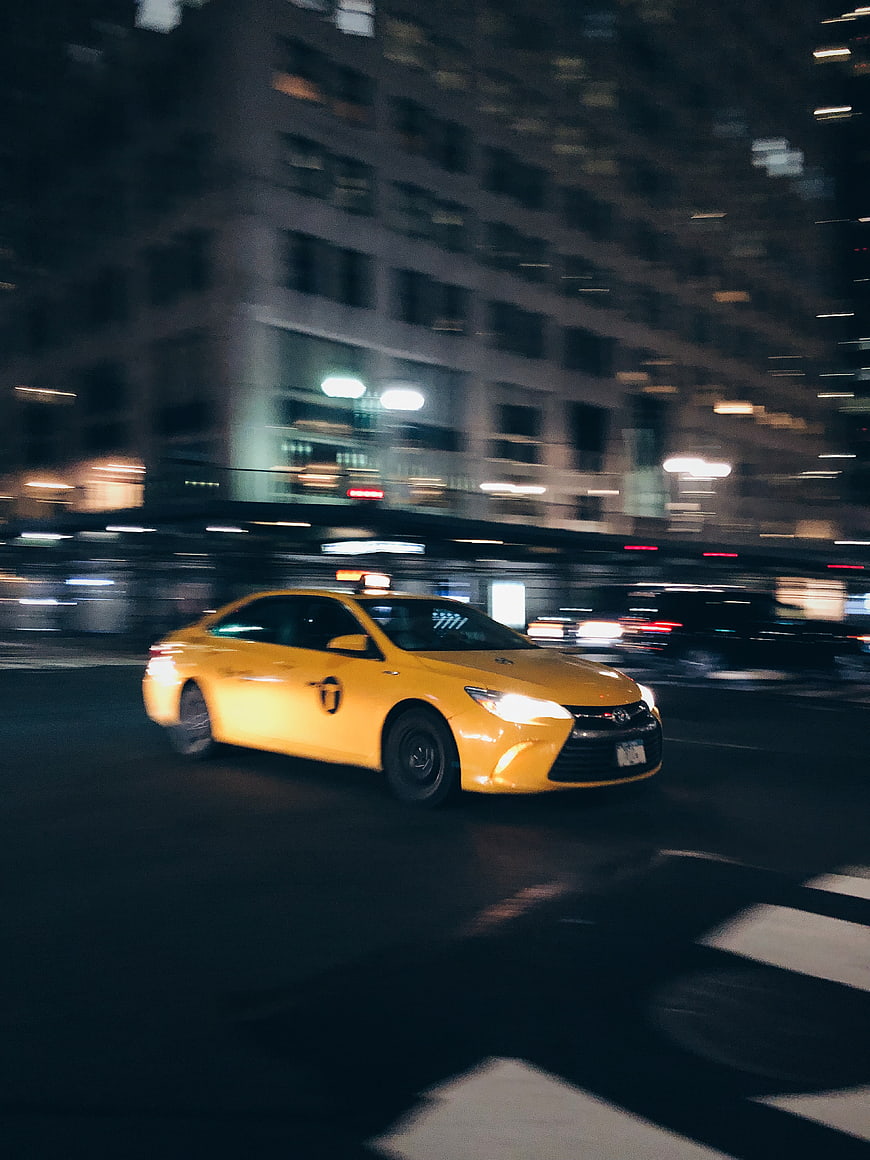 Yellow taxi driving fast through city streets at night